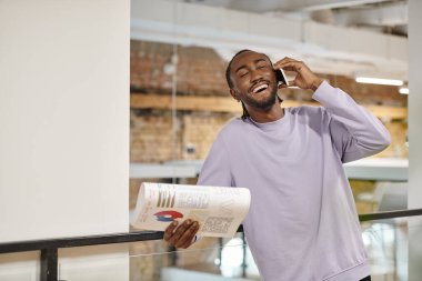 neşeli Afrikalı Amerikalı adam akıllı telefondan konuşuyor, gülüyor, başlıyor, grafik tutuyor, dijital