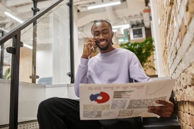Pozitif Afro-Amerikalı adamın elinde grafikler ve akıllı telefonla konuşması, merdivenlerde oturması, başlangıç