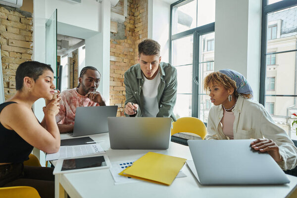 разнообразные коллеги, глядя на ноутбук, работая над стартап-проектом, идеи и планирование, офис