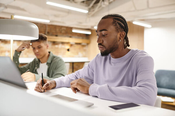 open space, african american man taking notes, writing down ideas near laptop, startup planning