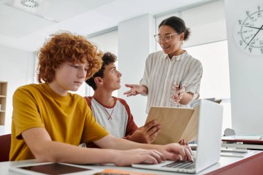 Gülümseyen Afro-Amerikan öğretmeni okulda aletlerle ders sırasında genç öğrencilerle konuşuyor.