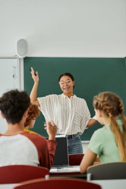 Pozitif Afro-Amerikan öğretmeni okulda dizüstü bilgisayarın yanında bulanık öğrencilerle konuşuyor.