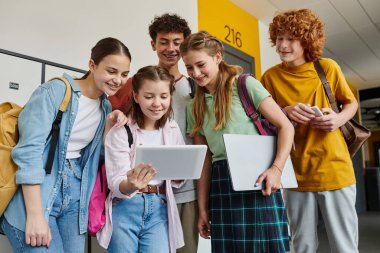 Genç öğrenciler dijital tablete bakıyor ve koridorda, teknolojide ve gençlerde duruyorlar.