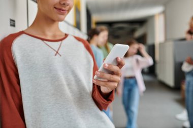 Akıllı telefon tutan mutlu okul çocuğunun görüntüsü, okul molasında mesajlaşması, bulanıklık.
