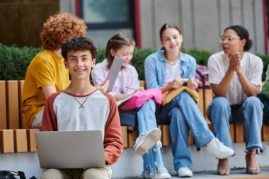 Okula dönen, kameraya bakan mutlu genç çocuk, dizüstü bilgisayar, çeşitlilik, öğretmen ve öğrenciler.