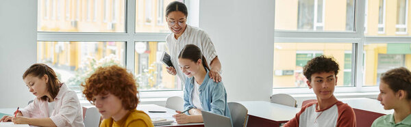 Позитивный африканский учитель-американец с цифровой табличкой, стоящей рядом с учениками в классе, баннер