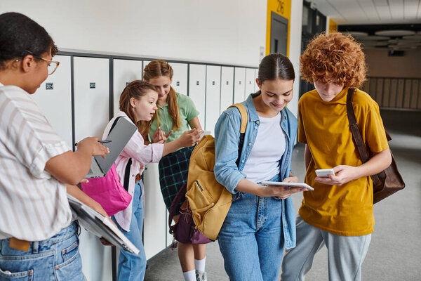 школьники-подростки с устройствами в школьном коридоре, африканская американка рядом со школьниками, черная женщина