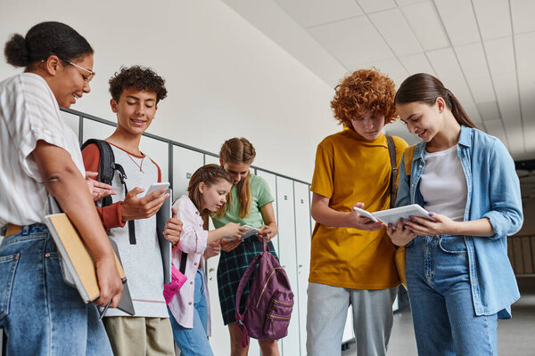 school hallway, african american teacher near teen student, schoolkids holding devices, digital age