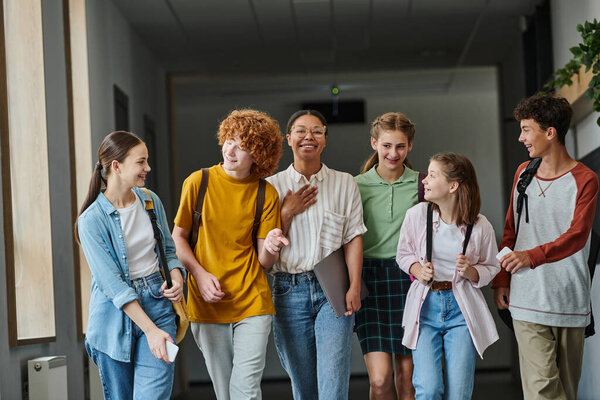 back to school, cultural diversity, teacher and teenage students walking in school hallway, smile