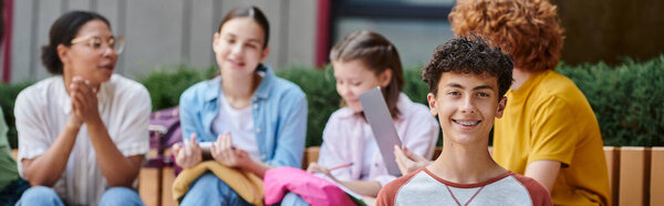banner, happy boy looking at camera near blurred classmates and teacher, diversity, education