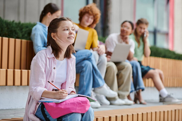 back to school, happy girl taking notes near teen classmates and teacher, blur, diversity, study