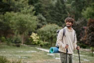 Neşeli Hintli sırt çantalı gezgin orman, seyahat ve macera konsepti üzerinde yürüyüş sopaları tutuyor.