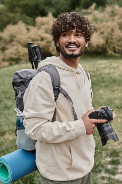 Sırt çantasında profesyonel kamera, macera ve yürüyüş taşıyan pozitif Hintli fotoğrafçı