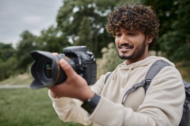 Sırt çantalı kıvırcık Hintli fotoğrafçı fotoğraf çekiyor profesyonel kamera, macera ve seyahat