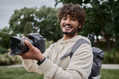 Sırt çantalı mutlu Hintli fotoğrafçı fotoğraf çekiyor profesyonel kamera, macera ve seyahat