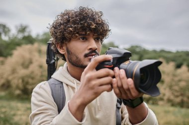 Profesyonel kamera kullanarak ve doğal mekanda fotoğraf çekerek konsantre Hintli fotoğrafçı