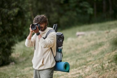 Kıvırcık Hintli turist profesyonel kamerada fotoğraf çekiyor, ormanda sırt çantalı gezgin, kaşif