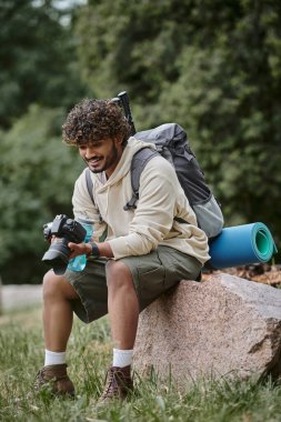 Profesyonel kamerayla gezen neşeli Hintli turist ve ormanda sırt çantalı bir adam.