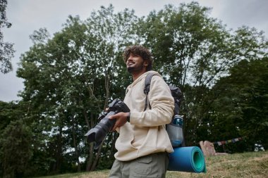 Kameralı mutlu Hintli adam ormanda sırt çantasıyla dikiliyor, fotoğrafçı.