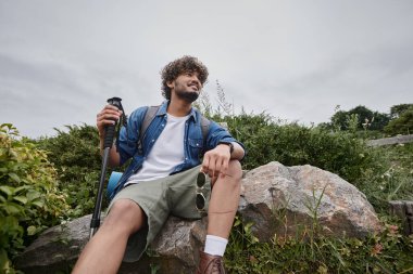 Sırt çantalı mutlu Hintli turist yürüyüş sırasında yürüyüş sopaları tutuyor, vahşi doğa.