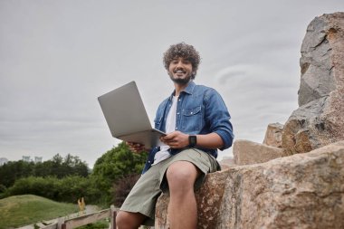 Uzaktan kumandayla çalışan mutlu Hintli serbest yazar ve bilgisayarı doğal yerde kullanıyor, dijital göçebelik.
