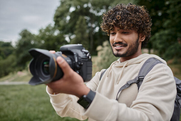 curly indian photographer with backpack taking photo on professional camera, adventure and travel