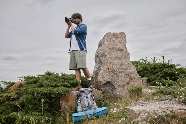 photography and nature concept, indian backpacker taking shot on digital camera and standing on rock