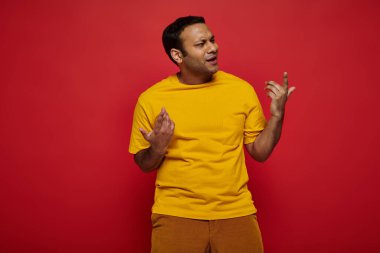 emotional indian man in bright casual clothes gesturing while explaining something on red background clipart