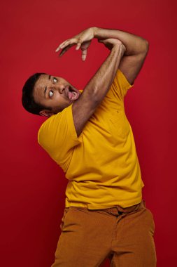 face expression, hand on shocked indian man in yellow t-shirt attacking him on red background clipart