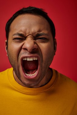 face expression, emotional indian man in yellow t-shirt screaming on red background, open mouth clipart