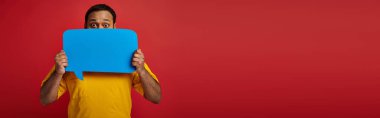 indian man with eyes wide open hiding behind blank speech bubble on red background, emotion, banner clipart