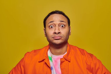 shocked indian man with eyes wide open looking at camera isolated on yellow, face expression clipart