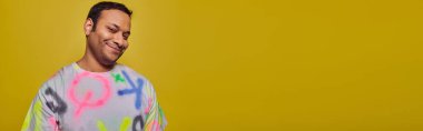 happy indian man in vibrant t-shirt smiling and looking at camera on yellow backdrop, style, banner clipart
