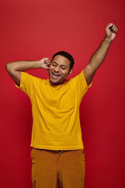 amazed indian man in bright casual clothes standing with raised hand on red background, yes gesture