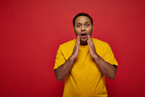 shocked indian man in bright casual clothes looking at camera on red background, open mouth