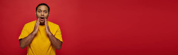 shocked indian man in bright casual clothes looking at camera on red background, open mouth, banner