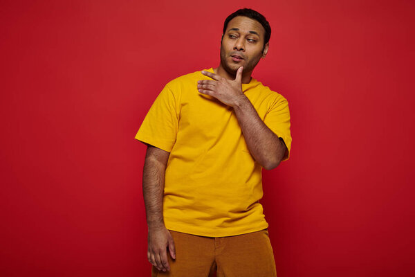 self-confidant haughty indian man in bright casual clothes grimacing on red background in studio