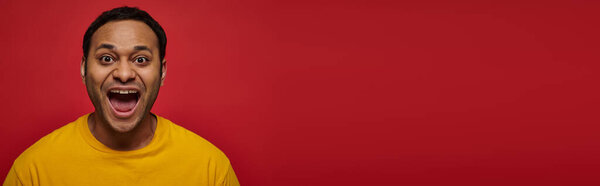 позитивные эмоции, возбужденный индиец в желтой футболке с открытым ртом на красном фоне, баннер