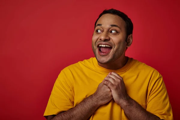 stock image astonished indian man with wide eyes open looking away on red background in studio, surprise concept