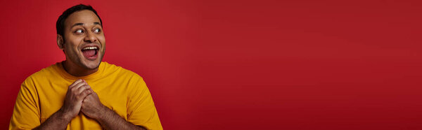 astonished indian man with wide eyes open looking away on red background, surprise concept, banner