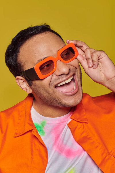 Концепция самовыражения, возбужденный индиец в ярко-оранжевых солнцезащитных очках, улыбающийся на желтом фоне