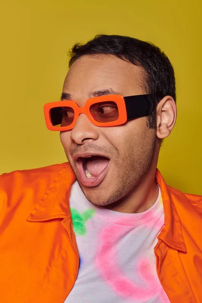 stock image self expression concept, excited indian man in orange sunglasses smiling on yellow backdrop
