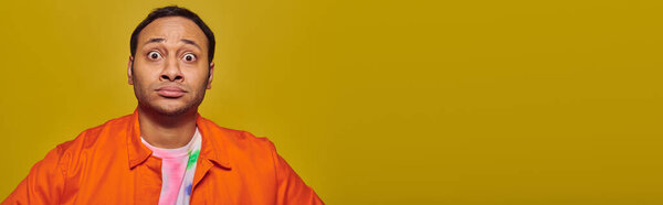 шокированный индиец с широко открытыми глазами смотрит на камеру, изолированную на желтом, выражение лица, баннер