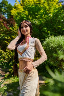 Seçkin geleneksel giysiler içinde genç ve memnun bir kadın yaz parkında gözlerini kaçırıyor.