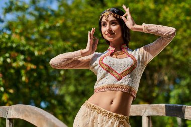 Neşeli Hintli kadın canlı geleneksel kıyafetleriyle güneşli yaz gününde parkta poz veriyor.