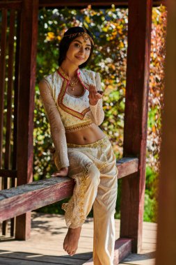 Yaz parkı, esmer kızılderili kadın canlı geleneksel giysiler içinde ahşap bölmede kameraya gülümsüyor.