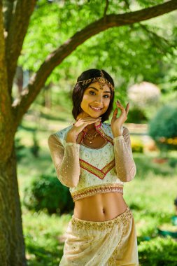 Geleneksel moda, yaz, mutlu Hintli kadın yeşil parkta dikilip kameraya bakıyor.