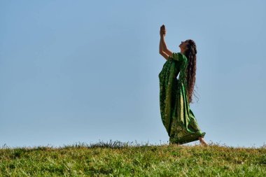 Yaz neşesi, otantik elbiseli Hintli kadın, dua eden elleri mavi gökyüzünün altındaki yeşil çimlerde.