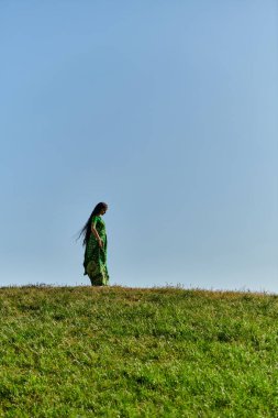 Yaz, etnik miras, yeşil tarlada mavi bulutsuz gökyüzü altında genç Hintli kadın