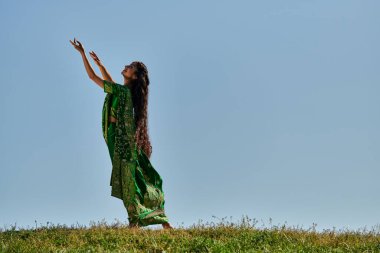 Yaz günü, otantik giyinmiş Hintli bir kadın uzanmış elleri mavi gökyüzünün altındaki yeşil tarlada